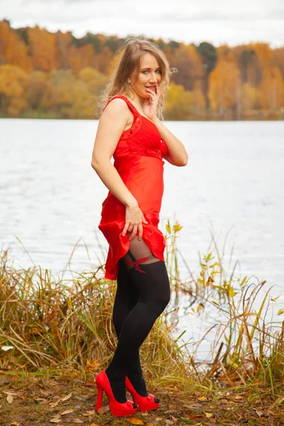 Mujer joven en vestido corto rojo y pantimedias negras caminando cerca del lago en el fondo del jardín de otoño solo —  Fotos de Stock