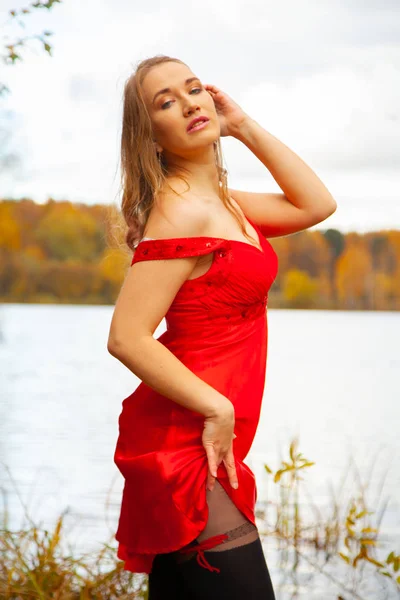 Jovem mulher em vestido vermelho curto e meia-calça preta andando perto do lago no fundo do jardim outono sozinho — Fotografia de Stock