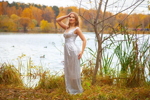 Hermosa chica de talla grande en vestido largo de plata posando cerca del estanque en la ciudad de otoño Parque solo — Foto de Stock