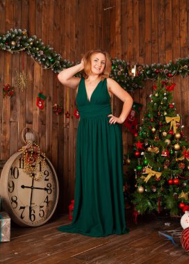 V yakalı uzun elbiseli zarif bir kadın. Noel ağacının yanında poz veriyor.