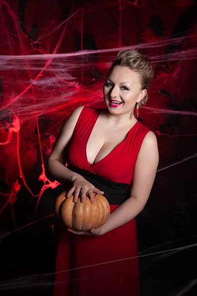 Vrouw in avond klassieke jurk poseren met pompoen op zwarte Halloween achtergrond met spinnenweb — Stockfoto