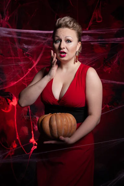Woman in evening classic dress posing with pumpkin on black Halloween background with spider web — Stock Photo, Image