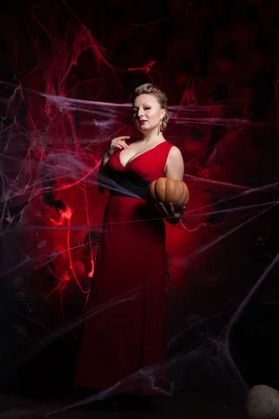 Frau in klassischem Abendkleid posiert mit Kürbis auf schwarzem Halloween-Hintergrund mit Spinnennetz — Stockfoto