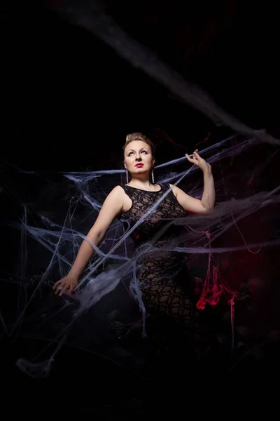 Perempuan dalam gaun klasik malam berpose pada latar belakang Halloween hitam dengan jaring laba-laba — Stok Foto