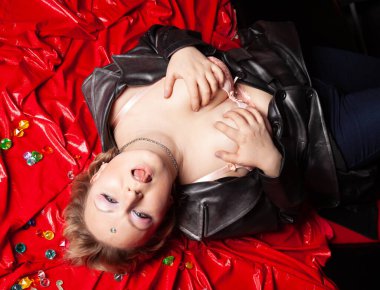 Güzel, deri elbiseli, iri yarı bir kadın kırmızı bir yatak örtüsünün üzerinde yatıyor. Yukarıdan görünüm.