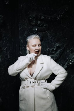 Genç ucube artı boyut albino kadın açgözlülükle yiyor ve siyah arka planda çikolatayı seviyor. kıvrımlı kısa saçlı beyaz elbiseli kız..