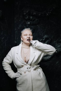 Genç ucube artı boyut albino kadın açgözlülükle yiyor ve siyah arka planda çikolatayı seviyor. kıvrımlı kısa saçlı beyaz elbiseli kız..