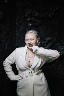 Genç ucube artı boyut albino kadın açgözlülükle yiyor ve siyah arka planda çikolatayı seviyor. kıvrımlı kısa saçlı beyaz elbiseli kız..