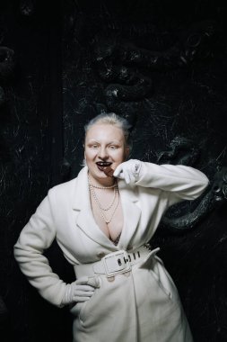 Genç ucube artı boyut albino kadın açgözlülükle yiyor ve siyah arka planda çikolatayı seviyor. kıvrımlı kısa saçlı beyaz elbiseli kız..