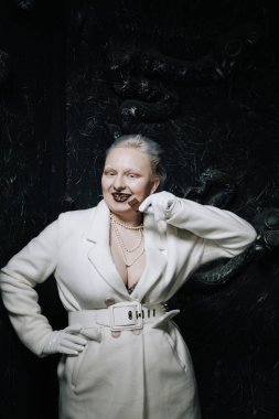 Genç ucube artı boyut albino kadın açgözlülükle yiyor ve siyah arka planda çikolatayı seviyor. kıvrımlı kısa saçlı beyaz elbiseli kız..