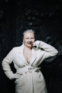 Genç ucube artı boyut albino kadın açgözlülükle yiyor ve siyah arka planda çikolatayı seviyor. kıvrımlı kısa saçlı beyaz elbiseli kız..