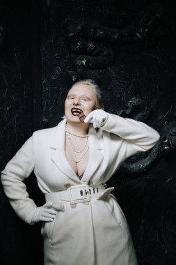 Genç ucube artı boyut albino kadın açgözlülükle yiyor ve siyah arka planda çikolatayı seviyor. kıvrımlı kısa saçlı beyaz elbiseli kız..