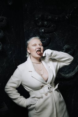 Genç ucube artı boyut albino kadın açgözlülükle yiyor ve siyah arka planda çikolatayı seviyor. kıvrımlı kısa saçlı beyaz elbiseli kız..