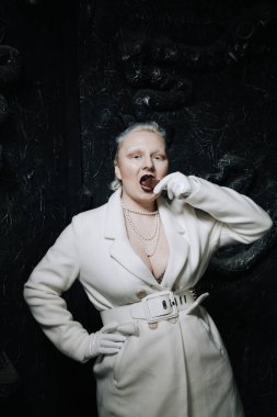 Genç ucube artı boyut albino kadın açgözlülükle yiyor ve siyah arka planda çikolatayı seviyor. kıvrımlı kısa saçlı beyaz elbiseli kız..