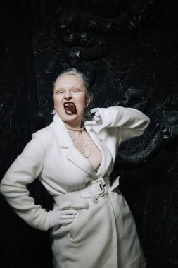 Genç ucube artı boyut albino kadın açgözlülükle yiyor ve siyah arka planda çikolatayı seviyor. kıvrımlı kısa saçlı beyaz elbiseli kız..