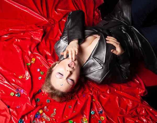 Güzel, deri elbiseli, iri yarı bir kadın kırmızı bir yatak örtüsünün üzerinde yatıyor. Yukarıdan görünüm.