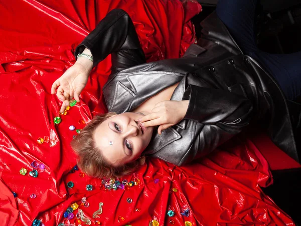 Güzel, deri elbiseli, iri yarı bir kadın kırmızı bir yatak örtüsünün üzerinde yatıyor. Yukarıdan görünüm.