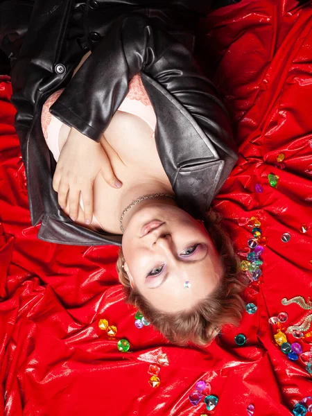 一个穿着皮衣的漂亮而又大的女人躺在红色的乙烯床单上。 从上往下看. — 图库照片