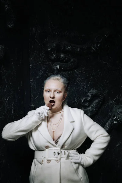 Young freak plus size albino woman greedily eats and love chocolate on black background. curvy short hair girl in white outfit. — Stock Photo, Image