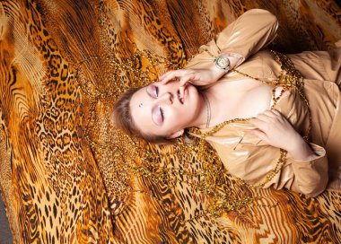 Çekici ve kısa saçlı bir kızın üst görüntüsü leopar desenli bir çarşafta deri bir ceketle yatıyor.