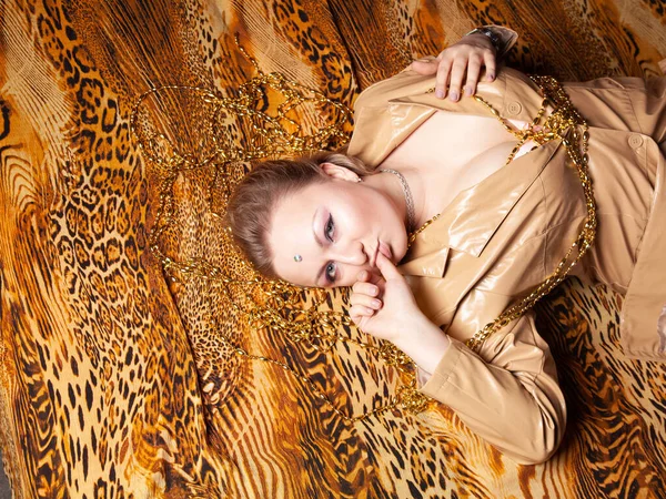 Vista superior na encantadora menina plus size com cabelo curto encontra-se em jaqueta bege de couro em uma folha de impressão de leopardo — Fotografia de Stock