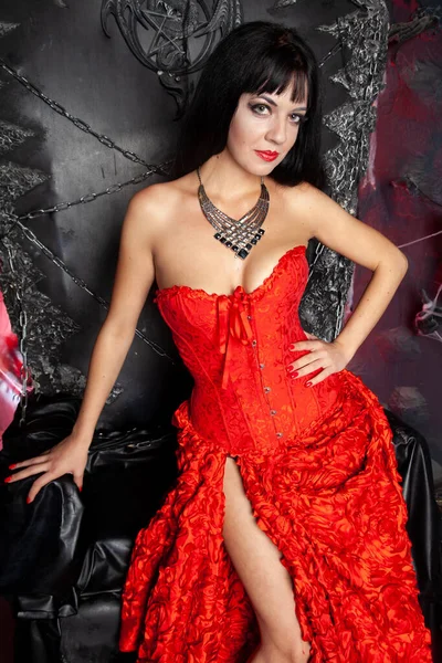 Красивая женщина вампир в красном длинном платье рядом с большим черным троном в студии — стоковое фото