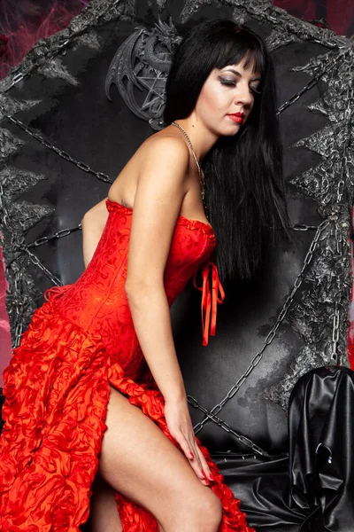 Bella donna vampiro in abito rosso lungo vicino grande trono nero in studio — Foto Stock