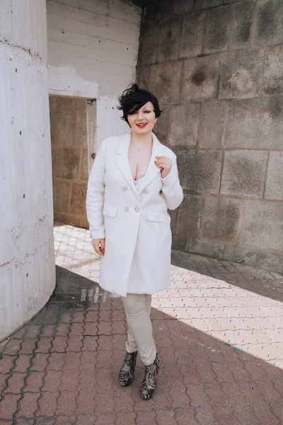 Young beautiful stylish woman in white wool coat walking down the street. Plus size short hair adult girl posing alone.
