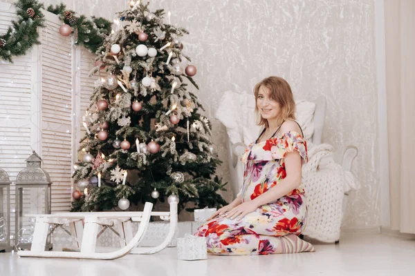 Mulher feliz grávida celebra o Natal no quarto decorado com abeto de ano novo — Fotografia de Stock