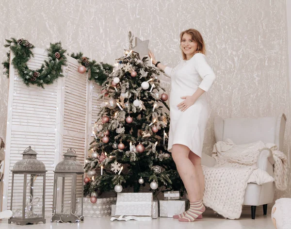 Mulher feliz grávida celebra o Natal no quarto decorado com abeto de ano novo — Fotografia de Stock