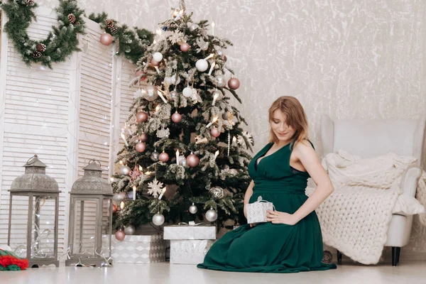 Mujer feliz embarazada celebra la Navidad en la habitación decorada con abeto de año nuevo — Foto de Stock