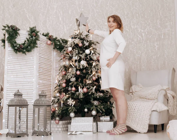 Mulher feliz grávida celebra o Natal no quarto decorado com abeto de ano novo — Fotografia de Stock