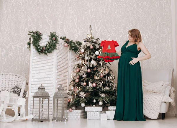 Těhotná šťastná žena slaví Vánoce v zdobené místnosti s novoroční jedlí — Stock fotografie