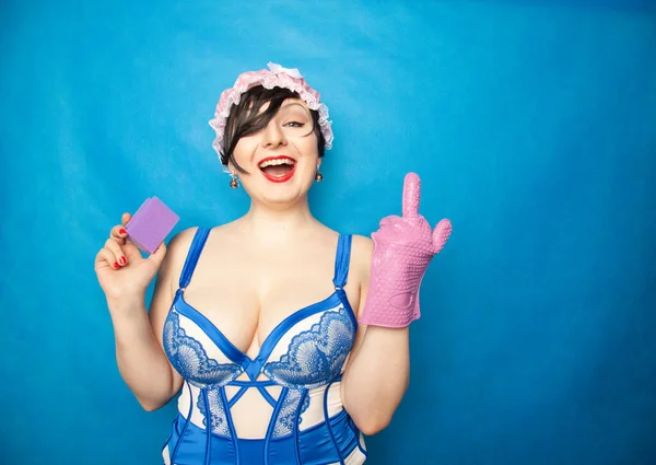 Schattig gelukkig plus size kort haar vrouw in blauw wit lingerie met een rubberen handschoen en een spons voor het wassen van de afwas op een solide achtergrond in Studio — Stockfoto
