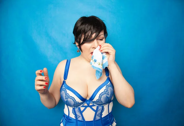 Красивая молодая женщина плачет от страданий аллергии и обычной простуды, вытирая слезы салфеткой на синем фоне — стоковое фото