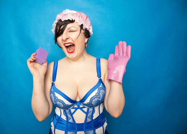 Прелестный счастливый плюс размер короткие волосы женщина в синем белом белье с резиновой перчаткой и губкой для мытья посуды на твердом фоне в студии — стоковое фото