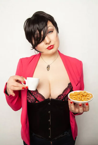 Plusz méretű lány rövid fekete haj áll egy csésze ital a kezében, és egy egészségtelen snack fehér háttér a stúdióban — Stock Fotó
