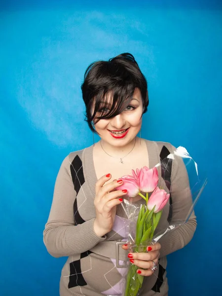 Beautiful girl in the cute sweater with flowers tulips in hands on a blue background — ストック写真