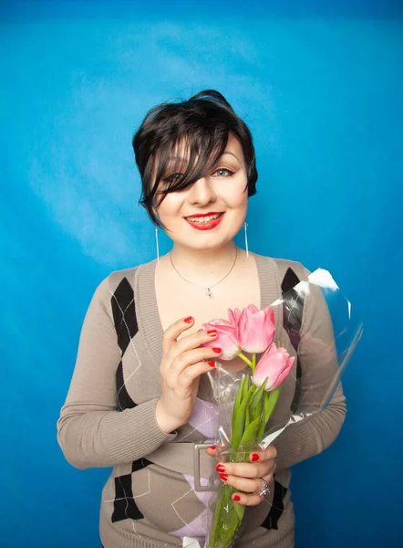 Hermosa chica en el suéter lindo con flores tulipanes en las manos sobre un fondo azul — Foto de Stock