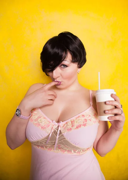 Jovem mulher bonita em vestido de lingerie rosa bebendo café no fundo amarelo — Fotografia de Stock