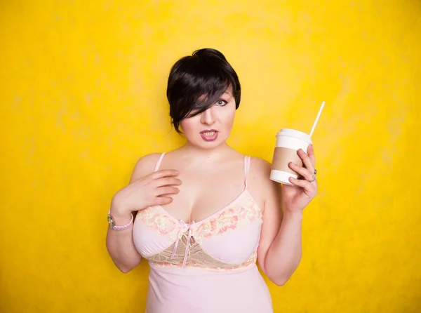 Jong mooi vrouw in roze lingerie jurk drinken koffie op gele achtergrond — Stockfoto