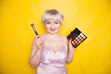 Makyaj seti ve fırçayla eğlenen mutlu, iri yarı bir kadın. Profesyonel çok renkli yüz düzeltme paleti.