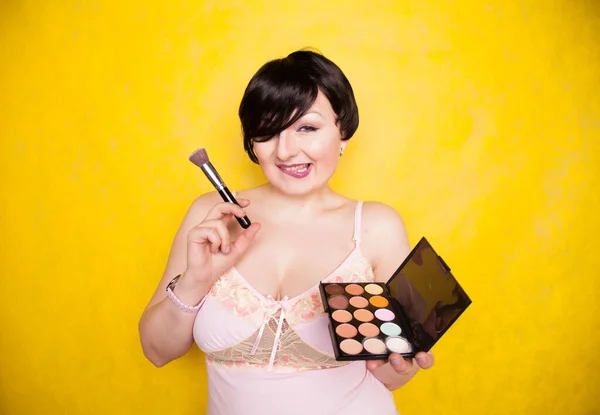 Feliz mulher plus size se divertindo com conjunto de paleta de maquiagem e escova. Paleta multicolorida profissional do corretor da cara da sombra . — Fotografia de Stock