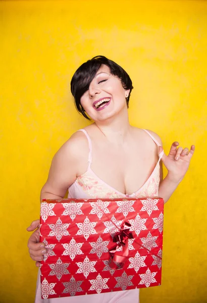 Happy Female holding in hands big gift with ribbon. Adult girl with red present on yellow studio background. — Stock Photo, Image