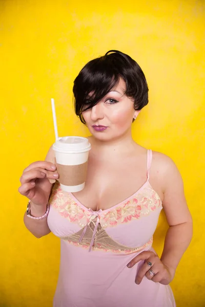 Fiatal csinos nő rózsaszín fehérnemű ruha iszik kávé sárga háttér — Stock Fotó