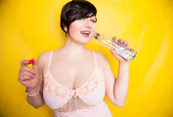 Beautiful woman going to drink some water from plastic bottle on yellow background in the studio alone — Stock Photo, Image