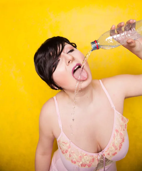 아름다운 여성 이 스튜디오에 있는 노란색 배경의 플라스틱 병에서 물을 마시려 합니다 — 스톡 사진