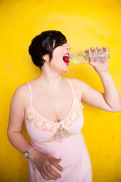 スタジオだけで黄色の背景のペットボトルから水を飲む美しい女性は — ストック写真