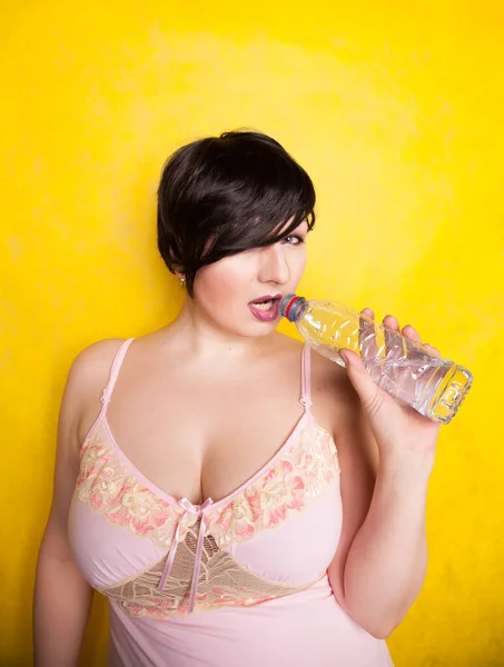 Hermosa mujer va a beber un poco de agua de botella de plástico sobre fondo amarillo en el estudio solo — Foto de Stock