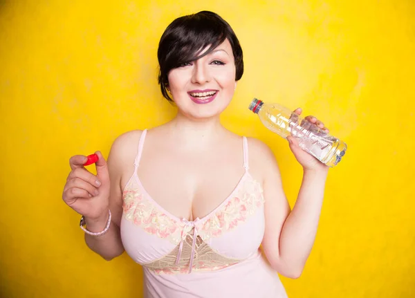 Красивая женщина собирается выпить немного воды из пластиковой бутылки на желтом фоне в студии в одиночку — стоковое фото